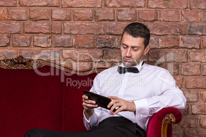businessman lying on a settee and reading tablet