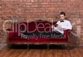 businessman lying on a settee and reading tablet