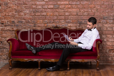 businessman lying on a settee and reading paperwork