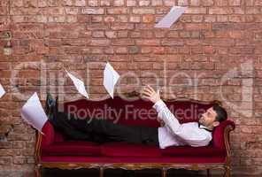 businessman lying on a settee with flying papers