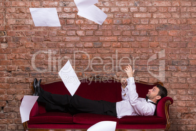 businessman lying on a settee with flying papers