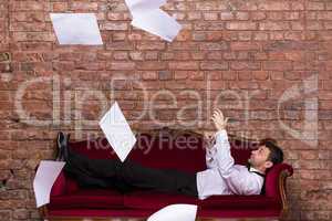 businessman lying on a settee with flying papers