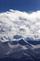 winter mountains in evening and silhouette of paraglider