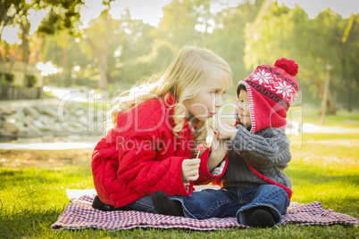little girl with baby brother wearing coats and hats outdoors.