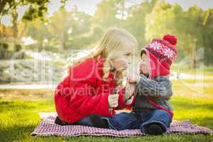 little girl with baby brother wearing coats and hats outdoors.