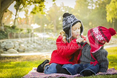 little girl with baby brother wearing coats and hats outdoors.