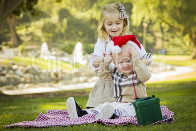 little girl tries to put santa hat on baby brother.