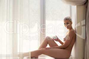 Nude girl drinking coffee sitting on windowsill