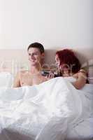 Happy young couple watching TV while lying in bed