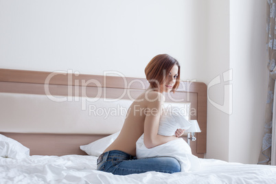 Smiling topless girl posing with pillow on bed