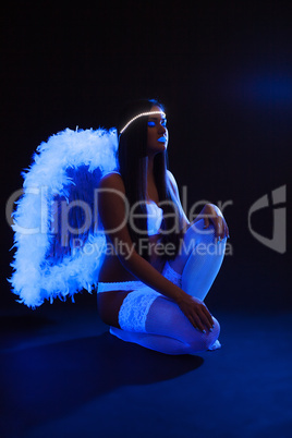 Sexy slim girl with UV makeup posing as angel