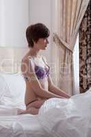 Profile of sensual young brunette sitting on bed