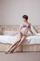 Model posing in purple lingerie, sitting on bed