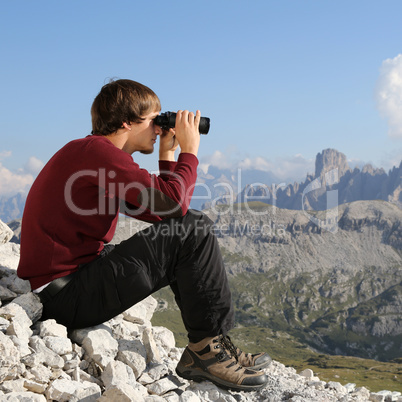 Junger Mann schaut in Bergen durch Fernglas