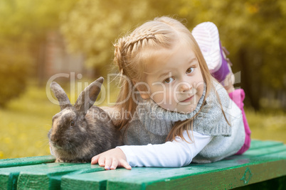 Cute brown-eyed girl lying on bench with rabbit