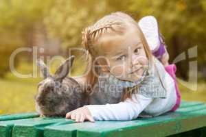 Cute brown-eyed girl lying on bench with rabbit