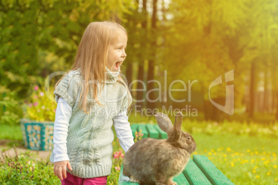 Cheerful little girl walking with rabbit in park