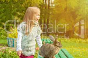 Cheerful little girl walking with rabbit in park