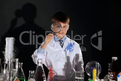 Smiling schoolboy looking through magnifying glass