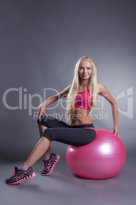 Confident pretty blonde posing with gymnastic ball