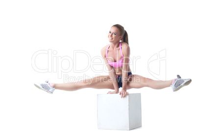 Smiling lovely sportswoman doing split on cube