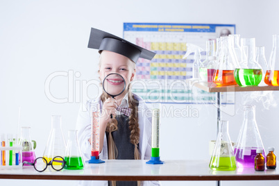 Funny little girl posing with magnifier in lab