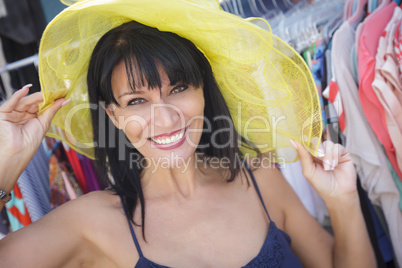 pretty italian woman trying on yellow hat at market