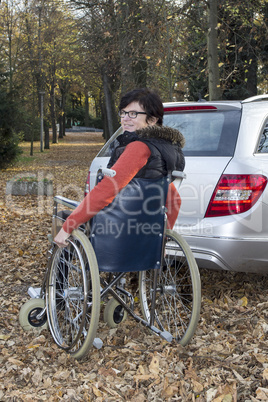 woman in a wheelchair in the fall next to their car