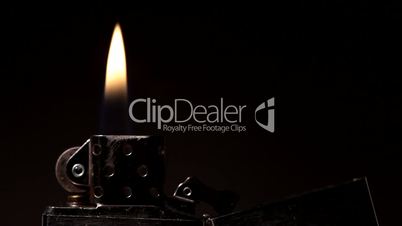 Open metal lighter with flame on black background