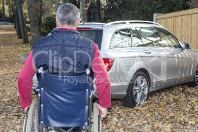 man in a wheelchair in the fall next to their car