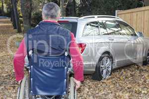 man in a wheelchair in the fall next to their car