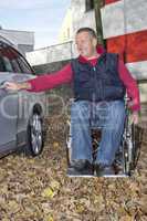 man in a wheelchair in the fall next to their car