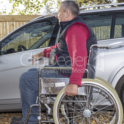 man in a wheelchair in the fall next to their car