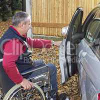 man in a wheelchair in the fall next to their car