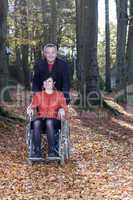 man pushing a wheelchair user in autumnal park