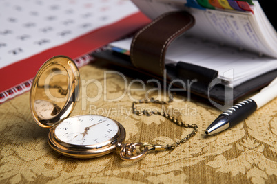 gold pocket watch and a wall calendar and sketchpad