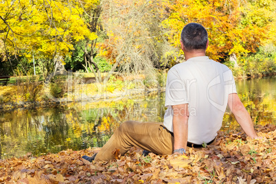 man sitting in autumn leaves by the lake