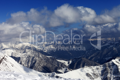 sunlit winter mountains in clouds, view from off-piste slope