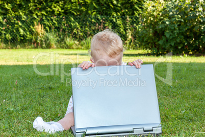 baby sitting with laptop in a meadow