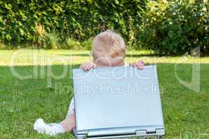 baby sitting with laptop in a meadow