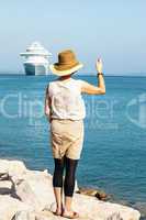 woman with hat stands on the sea and waves, a cruise ship