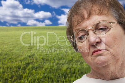 Melancholy Senior Woman with Grass Field Behind
