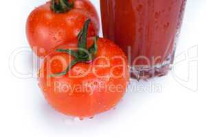 red tomatoes and glass of tomato juice on a white background
