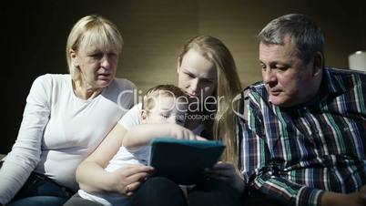 family watching boy playing game on touchpad