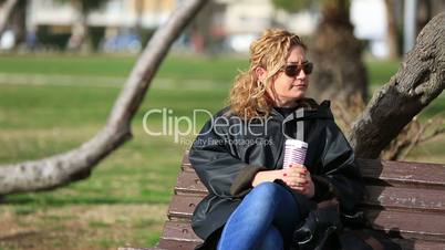 thoughtful blonde women sitting a bank and drink coffeee
