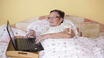 Senior woman with laptop in bed