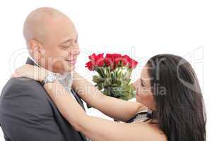 happy couple hugging with a bouquet of red roses in the middle.