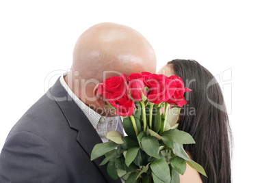 two young dates kissing behind a bouquet of red roses