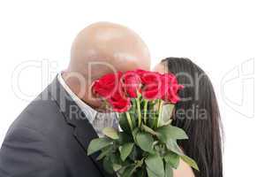 two young dates kissing behind a bouquet of red roses