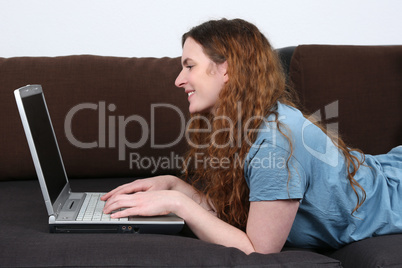 Junge Frau liegt auf Sofa und benutzt Laptop Computer